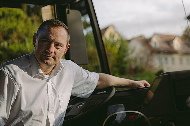 aufs Lenkrad gelehnter Busfahrer sieht freundlich aus der geöffneten vorderen Buseinstiegstüre
