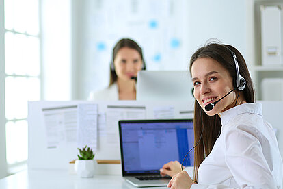 lächelnde Callcenter-Mitarbeiterin mit Headset und Computer im Büro